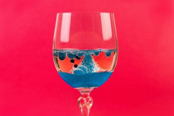Striking image of a glass with blue liquid on a red background