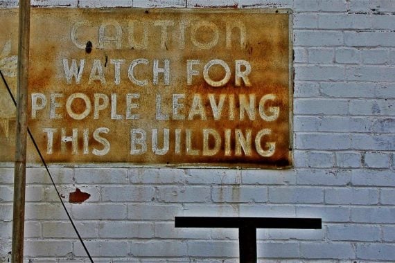 'Caution watch for people leaving the building' sign on brick wall