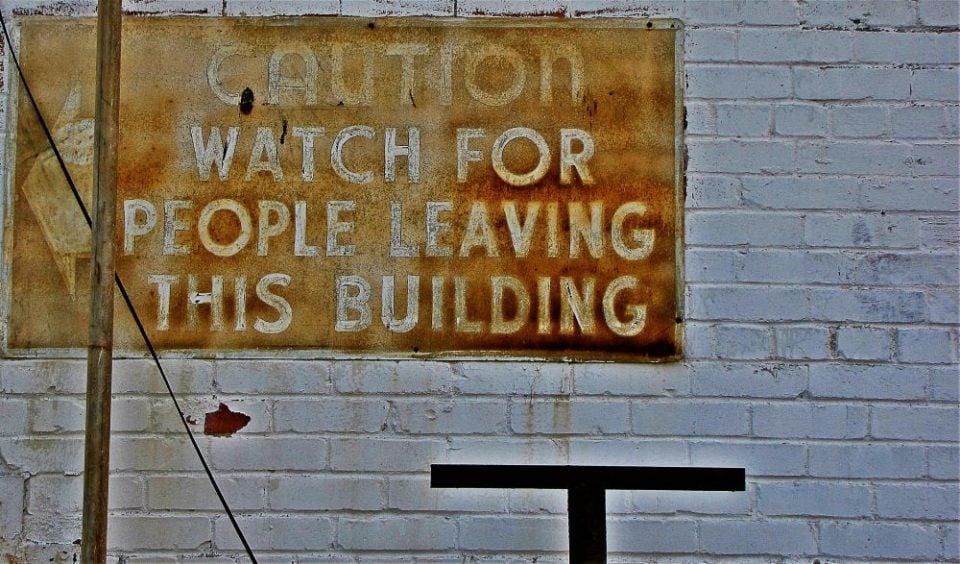 'Caution watch for people leaving the building' sign on brick wall