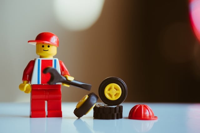 A yellow and red Lego figure holding a wrench and standing next to toy wheels