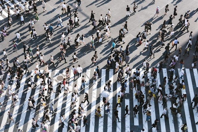 a busy zebra crossing picture taken at a high angle. Many pedestrians crossing the black and white crossing